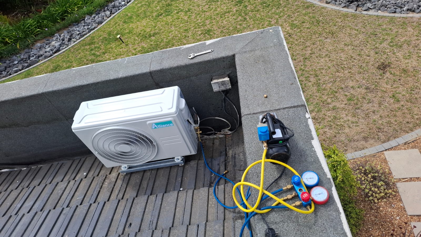 Vacuum pump and manifold gauges connected to an Alliance outdoor unit on a tiled roof