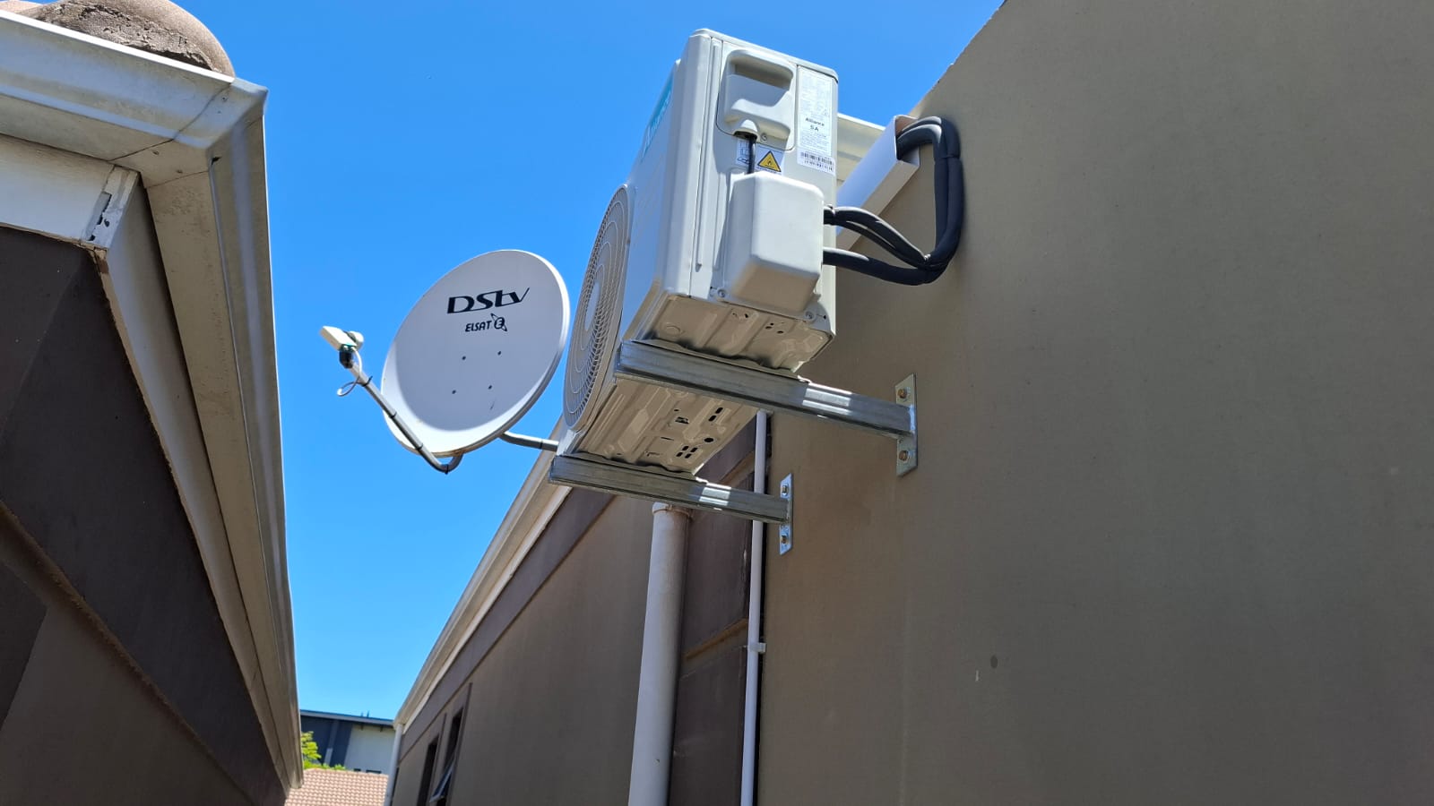 Alliance outdoor unit on a wall bracket beside a satellite dish