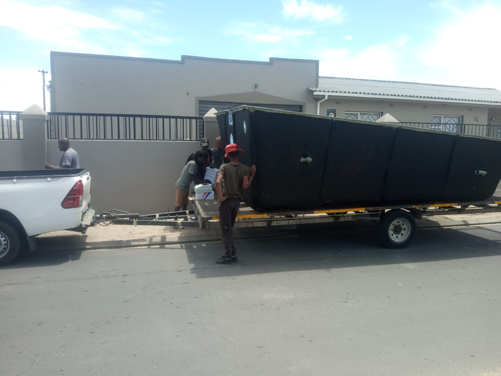 Fibreglass pool shell strapped to a flatbed trailer behind a bakkie