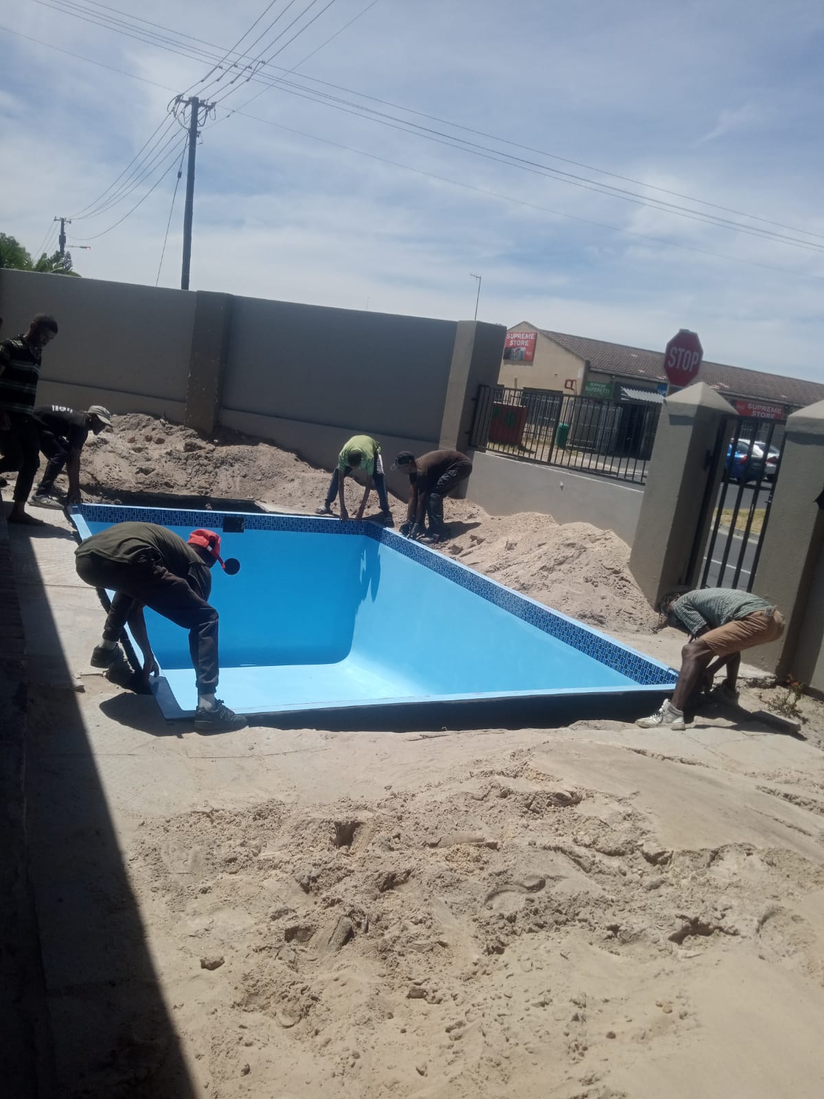 Team guiding a blue fibreglass pool shell down into a prepared excavation
