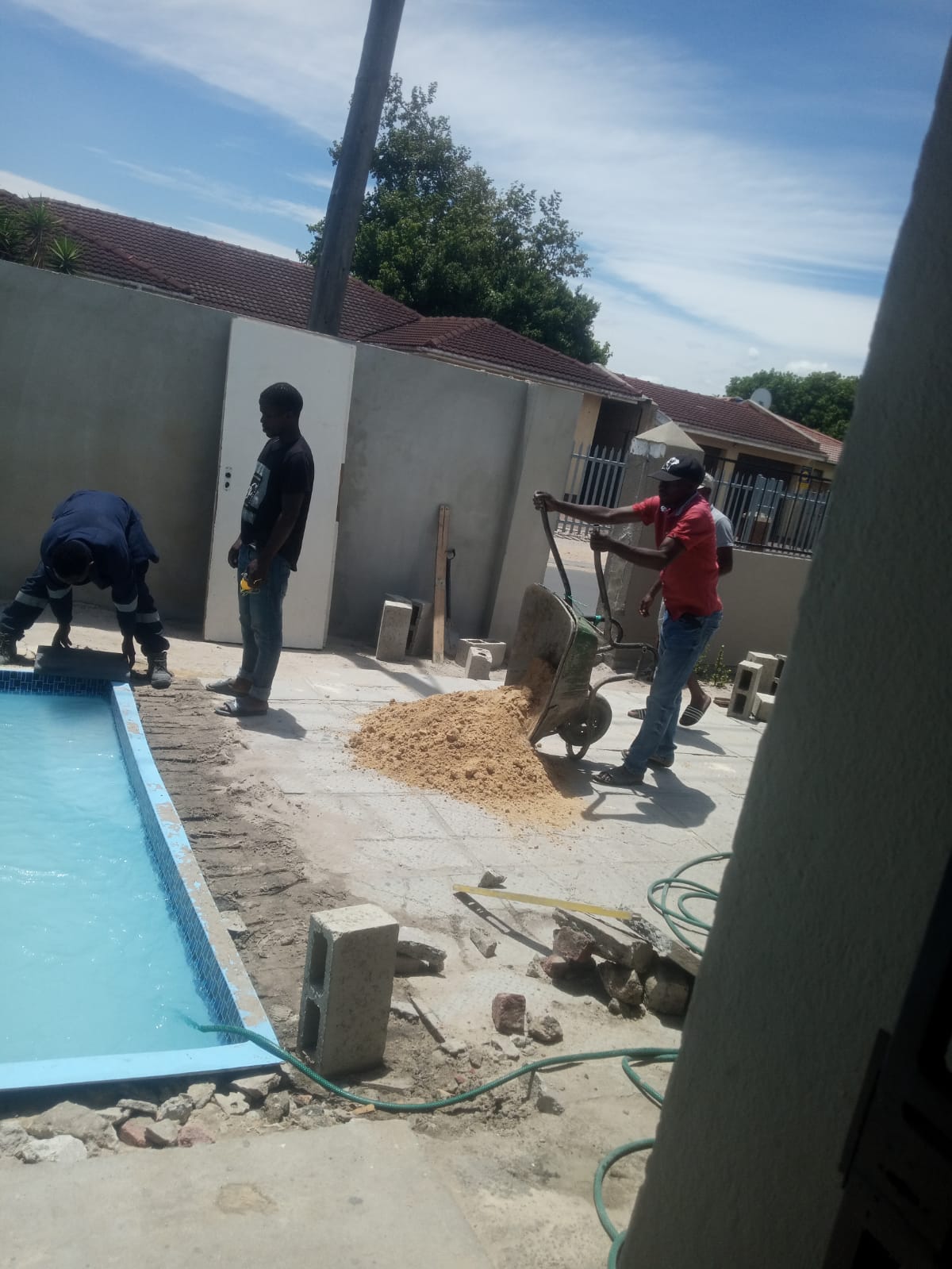 Coping slabs being laid around a newly installed pool while sand is barrowed in