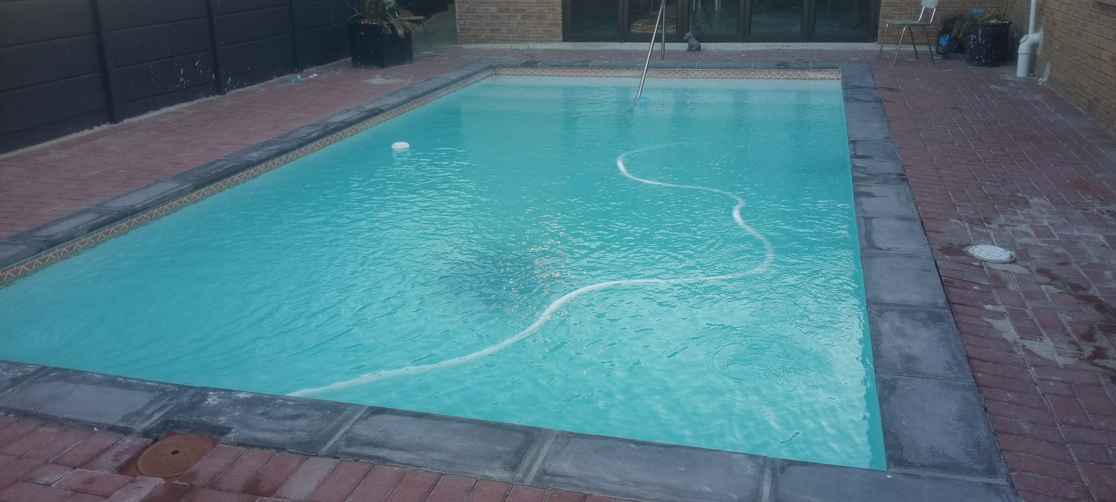 Clear blue pool with a suction cleaner hose running across the surface