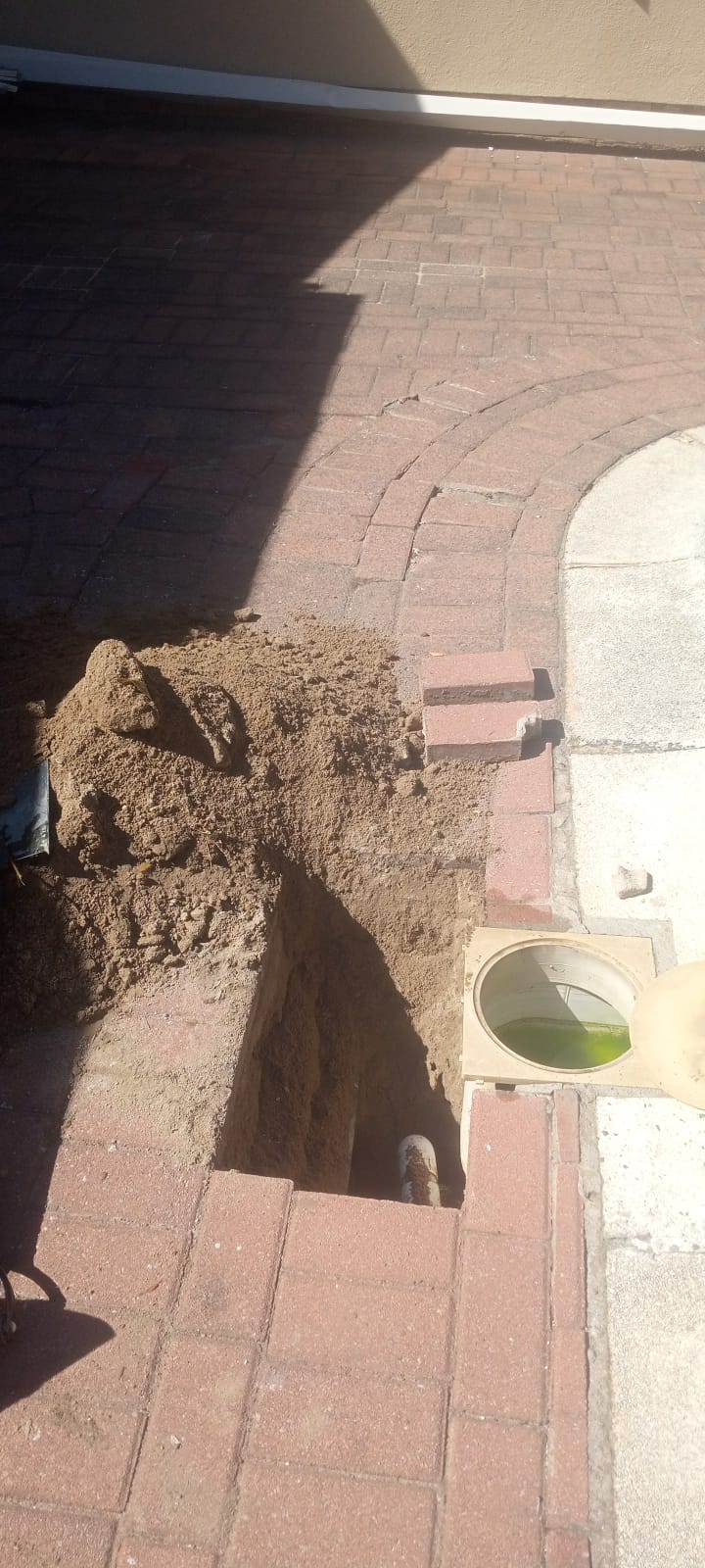 Excavation through brick paving exposing pool suction pipework beside a weir